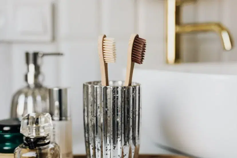 Eco friendly bamboo toothbrushes in silver glass placed in bathroom near sink and beauty products