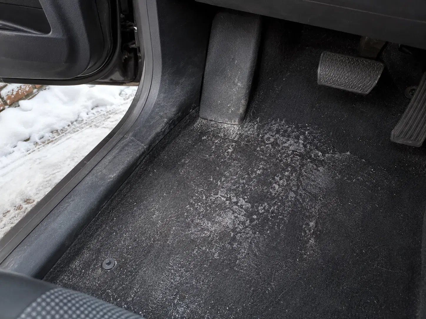 Salt-stained car footwell carpet in an Ottawa driveway with snow outside