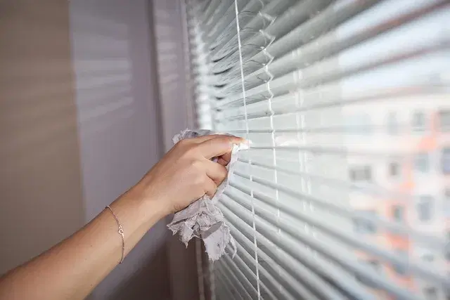 Hands cleaning window blinds with a cloth