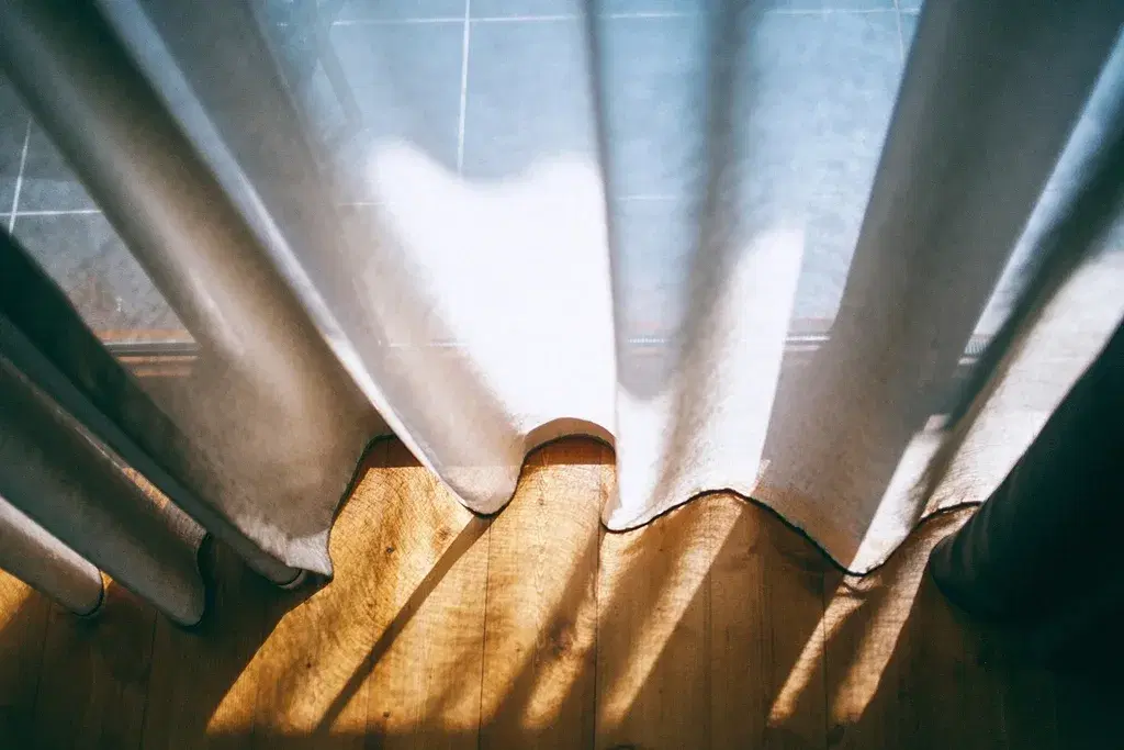 Spring sunlight streaming through sheer curtains onto a wooden floor