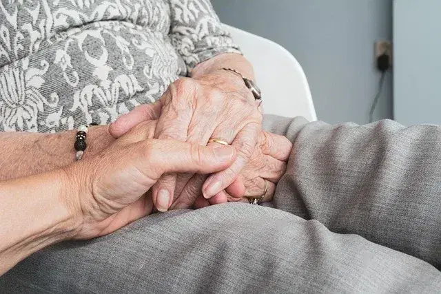 Adult child holding an aging parent's hands at home