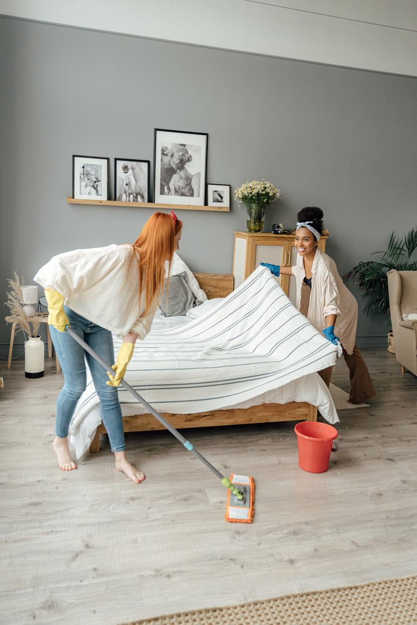 two women cleaning a bedroom with a mop